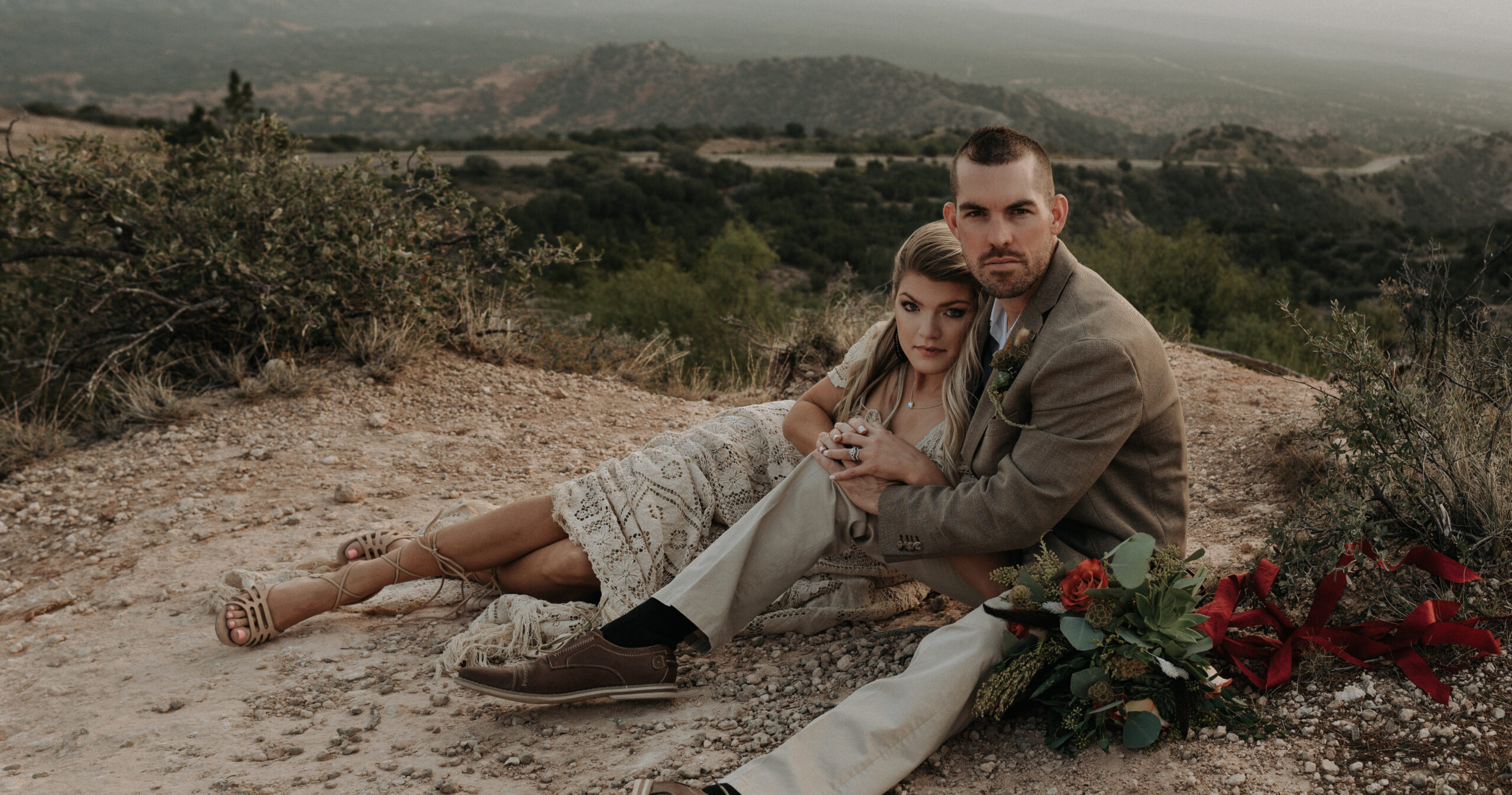 woman and man holding hands while sitting down on the cliffside of a canyon during their elopement photoshoot. elopement photography for a destination elopement photoshoot