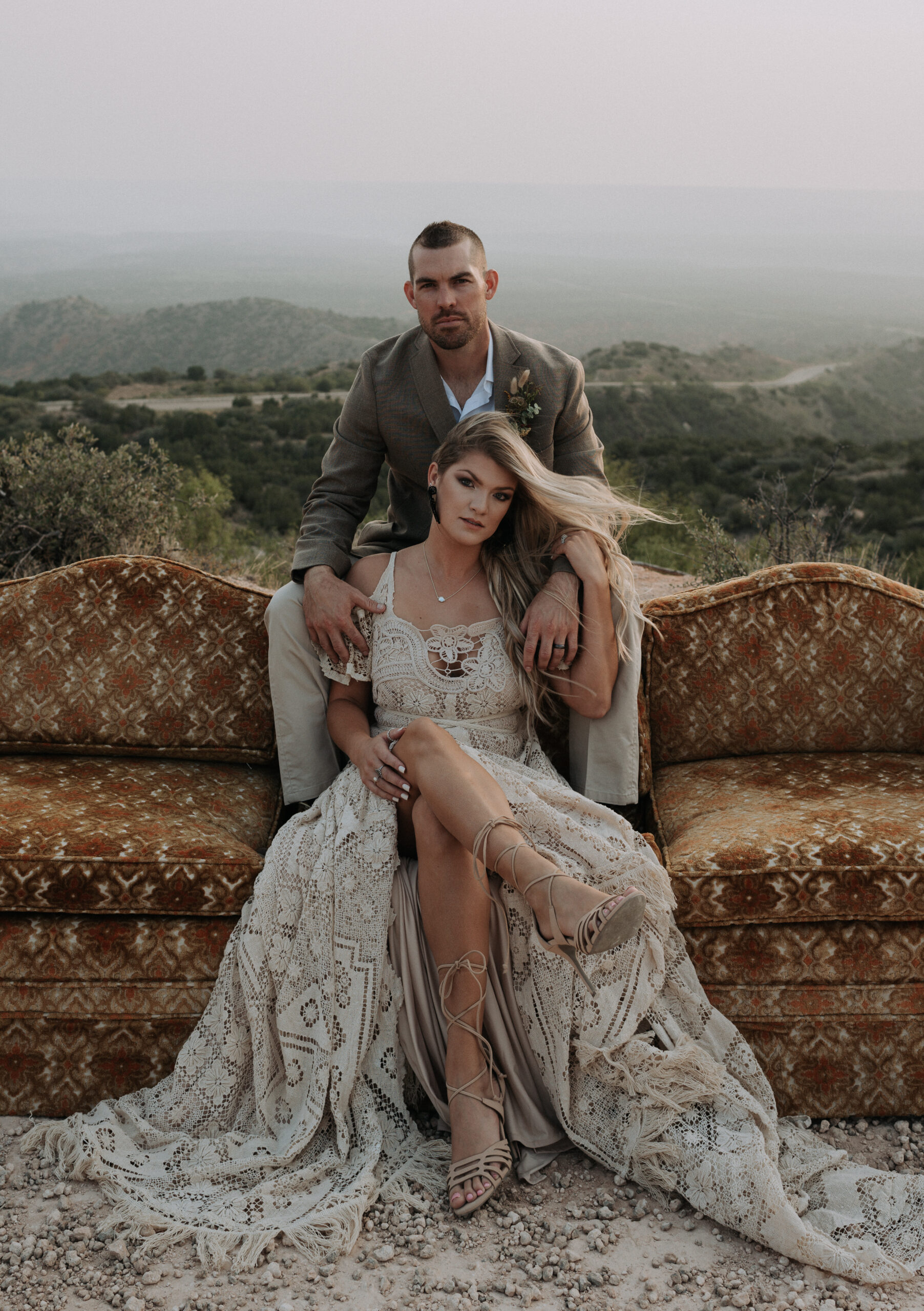 man and woman sitting on couch while posing for elopement photos with a background of a canyon. elopement photographer in texas for destination elopement photography