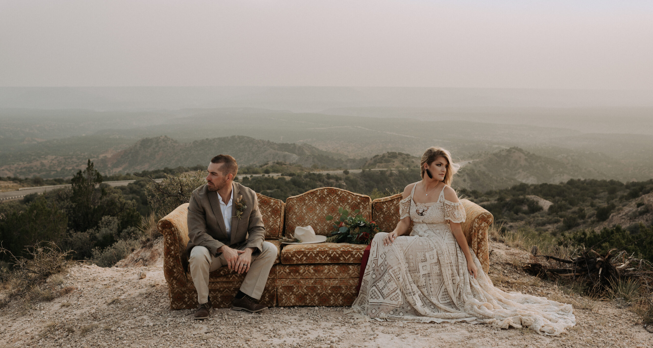 man and woman sitting on couch while posing for elopement photos with a background of a canyon. elopement photographer in texas for destination elopement photography