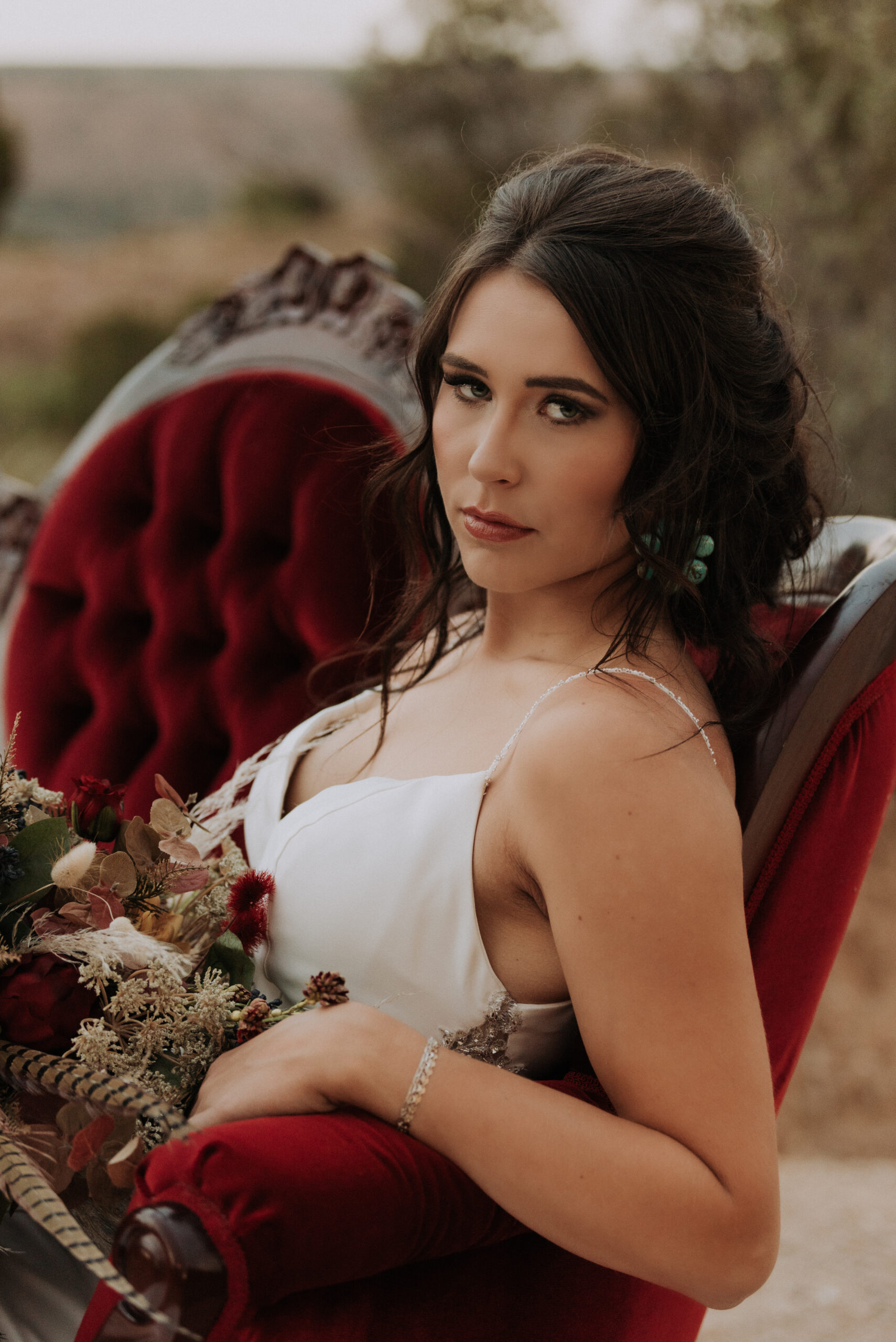 woman holding wedding bouquet while posing on settee and looking at camera, bridal portrait photographer Texas