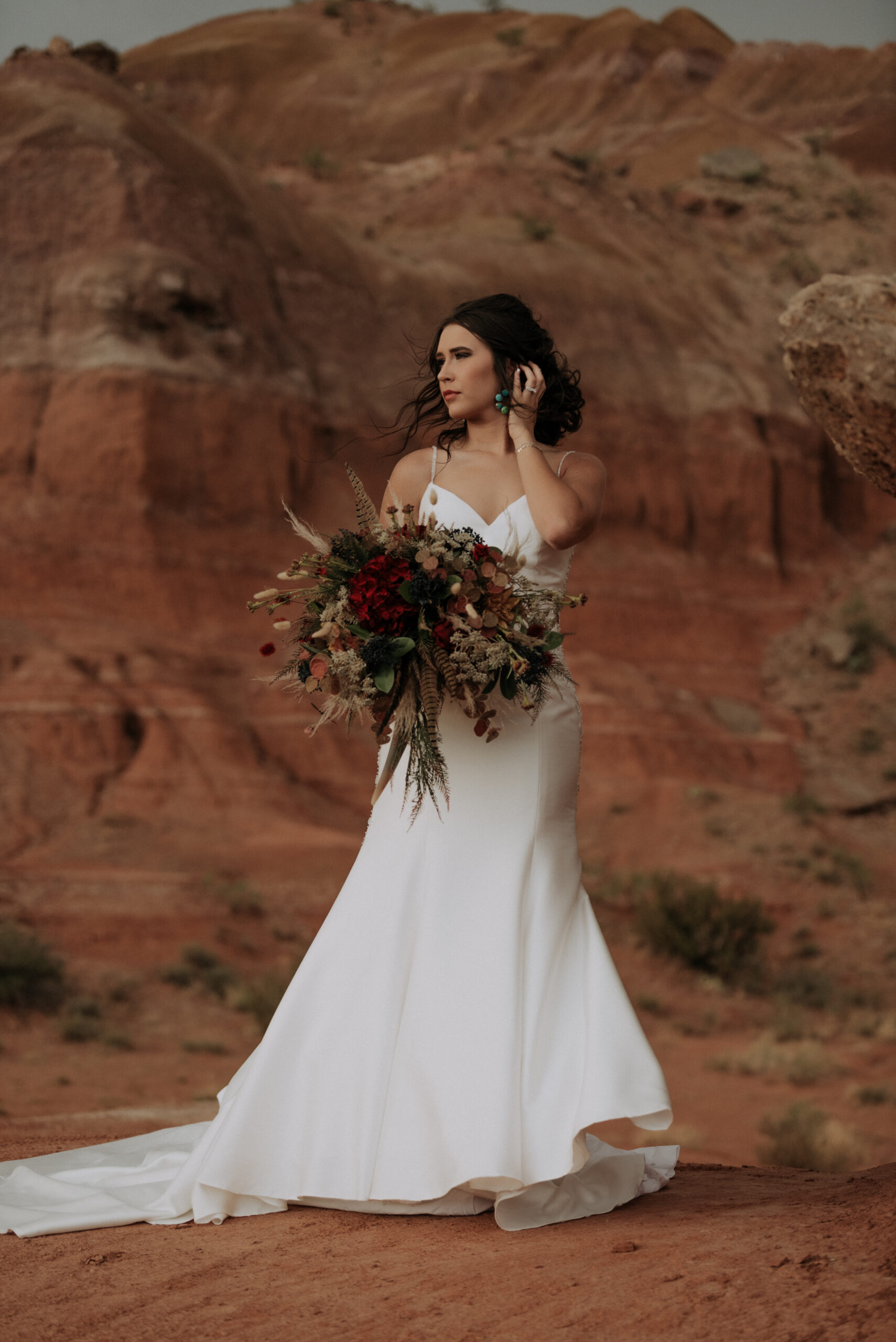 woman holding hand to hair while posing in the desert in Texas holding a wedding bouquet with wedding dress, Texas wedding photographer, bridal portrait session