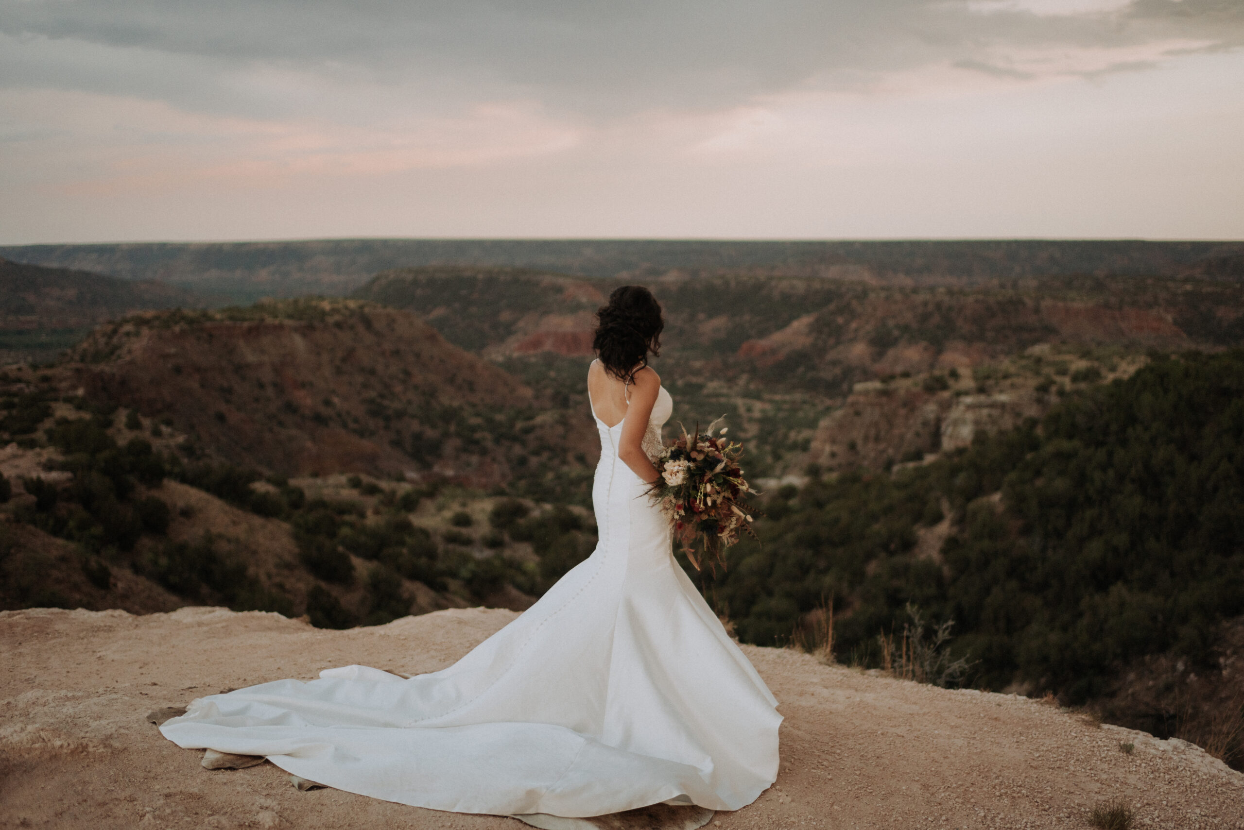 woman wearing wedding dress and overlooking desert while holding a wedding bouquet for bridal portrait photos. Texas wedding photographer and elopement photographer, bridal photos