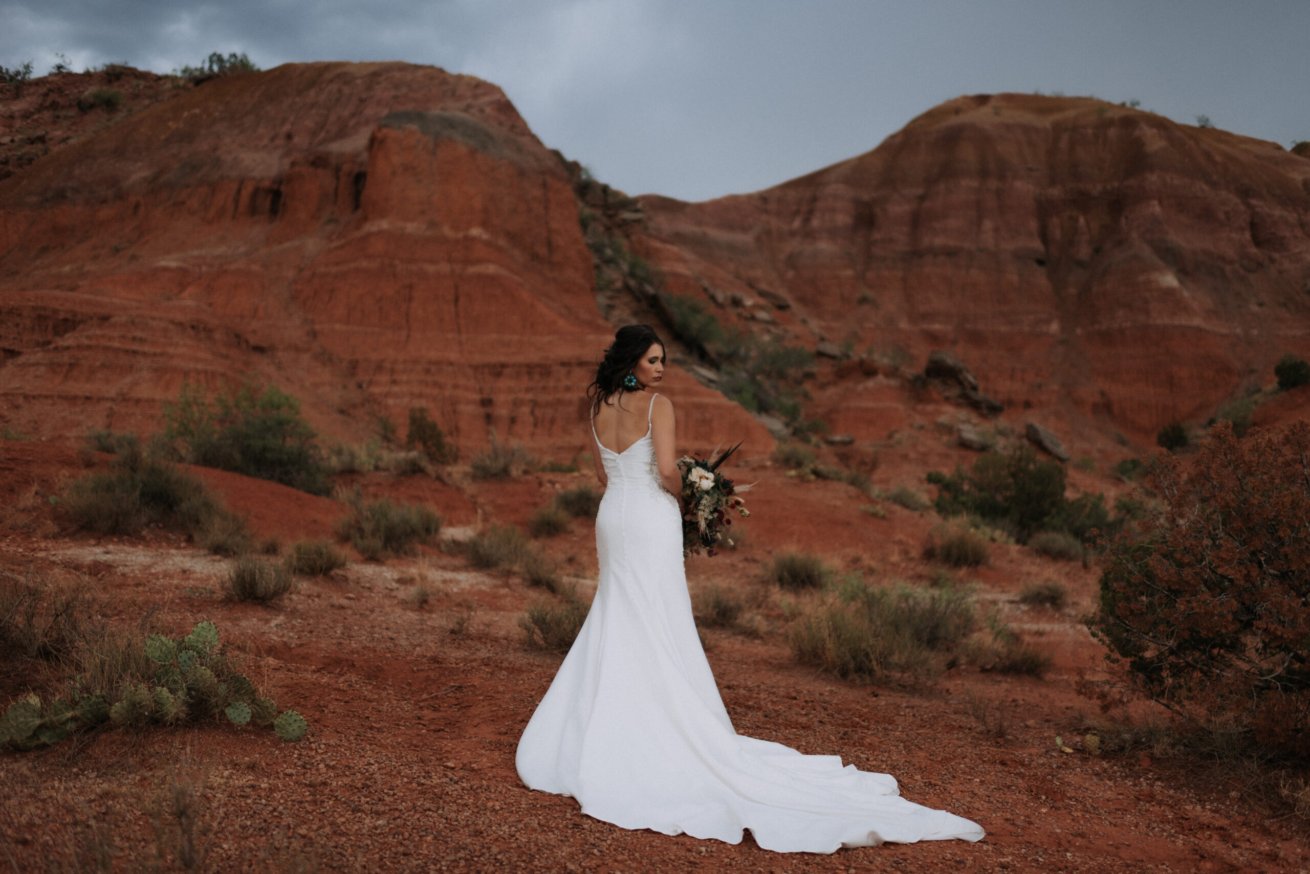 woman wearing wedding dress and posing looking at ground while holding wedding bouquet and turquoise earrings, Texas wedding photographer and bridal session photos